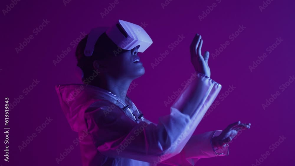 Woman in futuristic costume. Girl in glasses of virtual reality while touching air. Augmented reality game, future technology, AI concept. VR. Neon blue and red light. Dark background. Woman in futuristic costume. Girl in glasses of virtual reality while touching air. Augmented reality game, future technology, AI concept. VR. Neon blue and red light. Dark background.