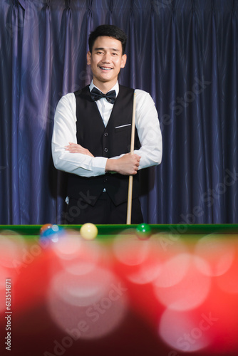 Foto Smiling Asian snooker player arms crossed holding snooker stick There is a red snooker ball in the foreground