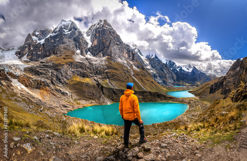 Man standing in front of a teal water lake with high Peruvian mountains in the Huayhuash mountain range, Peru photo