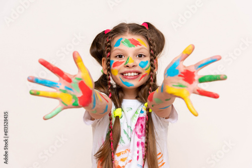 A little girl shows her palms painted with multicolored paints and smiles. A schoolgirl artist draws with her own hands. Creative education of children. White isolated background.