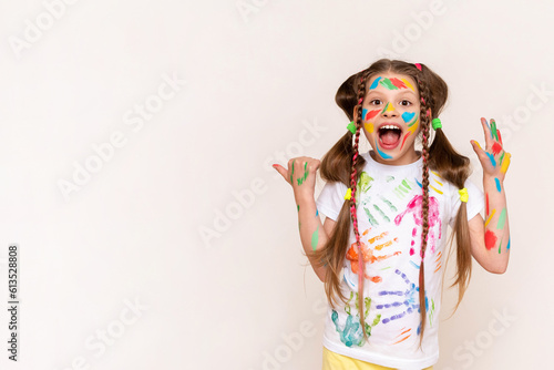 A little schoolgirl with painted hands and face with multicolored paints. A girl stained with paints. The concept of children's creativity. Funny child draws with his hands. Copy space. Banner.