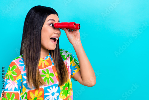 Photo of shiny impressed woman dressed flower print t-shirt looking binoculars empty space isolated blue color background