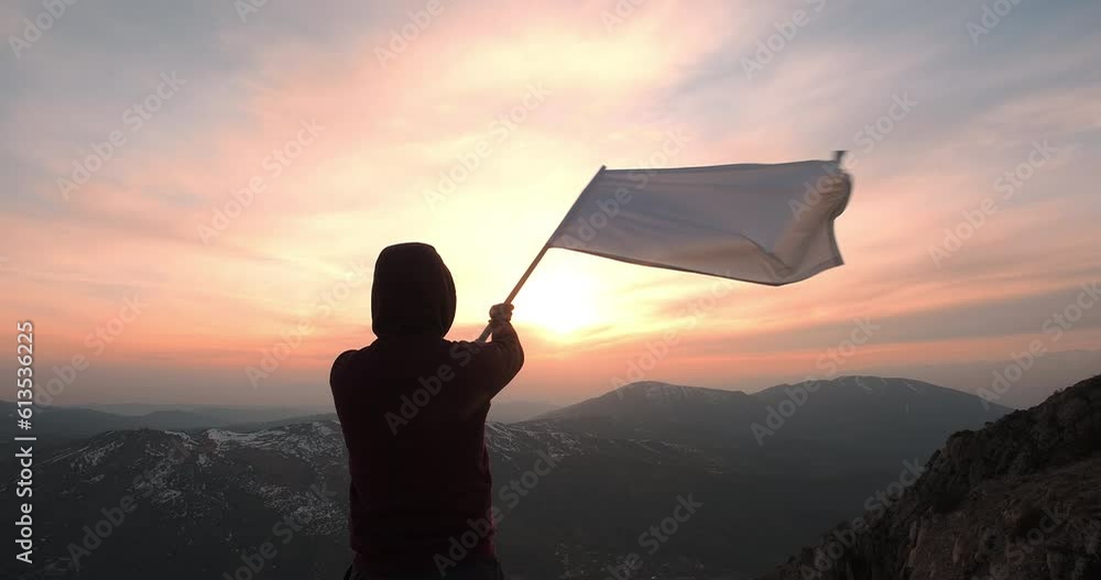 A man waving the white flag standing on the top of the mountain towards ...