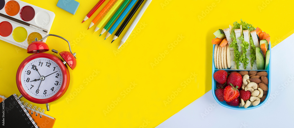 School stationery, red alarm clock and school lunchbox on the  yellow background.Top view. Copy space.