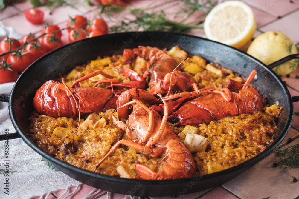 spanish seafood paella with lobster and squid, traditional dish with rice in a hot pot, surrounded by fresh ingredients on a pink background table, close up spanish seafood paella with lobster and squid, traditional dish with rice in a hot pot, surrounded by fresh ingredients on a pink background table, close up