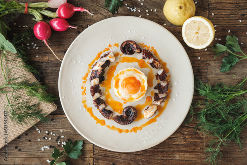 Fancy octopus dish on a plate, wooden rustic table, surrounded by fresh ingredients, top view photo