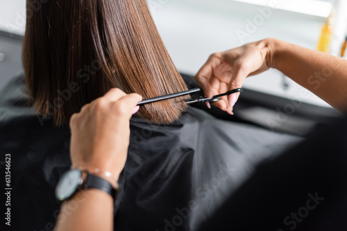 hairdo, cropped view of hairdresser cutting short brunette hair of female client, holding scissors and comb, professional, beauty worker, haircut, salon job, salon customer photo