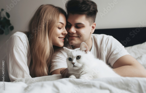 Happy smiling couple and their shaggy cat sitting on the bed  enjoying relaxed morning at home 