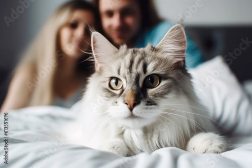 Happy smiling couple and their shaggy cat sitting on the bed, enjoying relaxed morning at home 