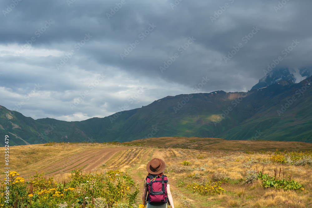 Woman in wide sun hat and backpack, tourist on hiking route to Koruldi Lakes, Svaneti region, Mestia Georgia. The concept of travel and active recreation. Summer day. Rear view