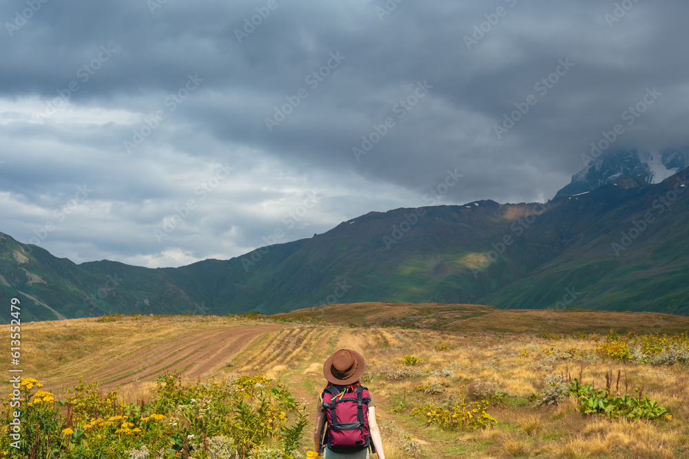 Woman in wide sun hat and backpack, tourist on hiking route to Koruldi Lakes, Svaneti region, Mestia Georgia. The concept of travel and active recreation. Summer day. Rear view Woman in wide sun hat and backpack, tourist on hiking route to Koruldi Lakes, Svaneti region, Mestia Georgia. The concept of travel and active recreation. Summer day. Rear view