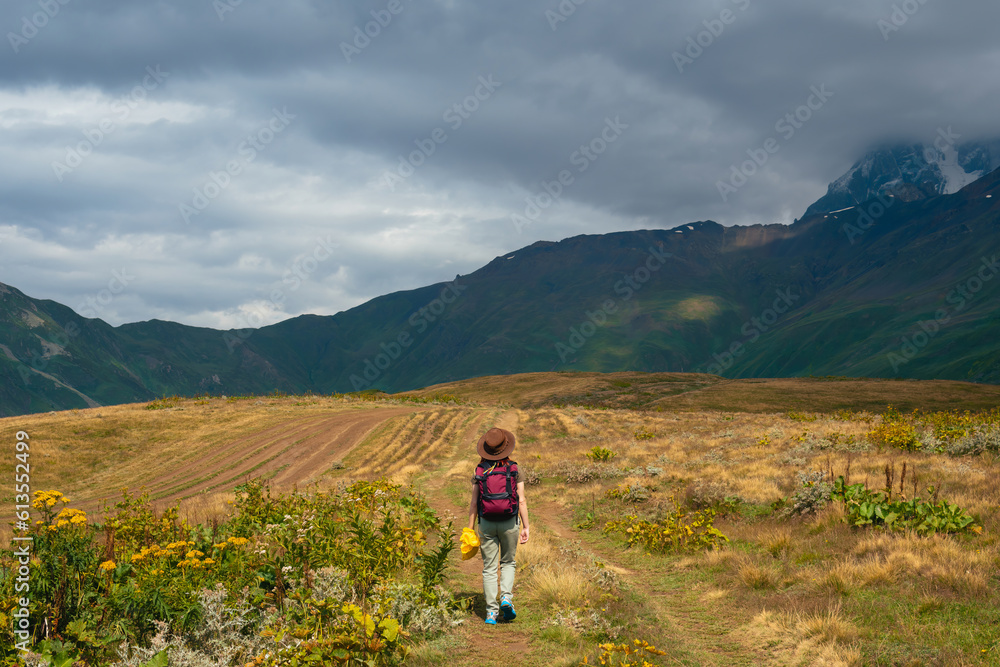 Woman in wide sun hat and backpack, tourist on hiking route to Koruldi Lakes, Svaneti region, Mestia Georgia. The concept of travel and active recreation. Summer day. Rear view Woman in wide sun hat and backpack, tourist on hiking route to Koruldi Lakes, Svaneti region, Mestia Georgia. The concept of travel and active recreation. Summer day. Rear view