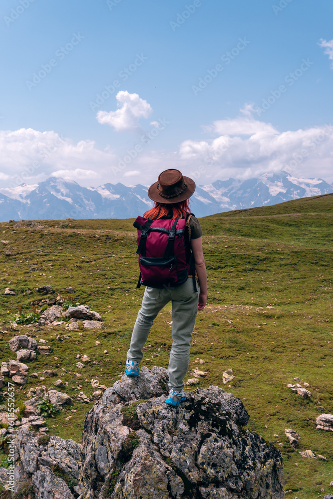 A woman, a tourist, a traveler stands on a boulder of a rock. End point of the walking route to Koruldi Lakes, Svaneti region, Georgia. Summer day in the mountains of the Caucasus. Vertical photo
