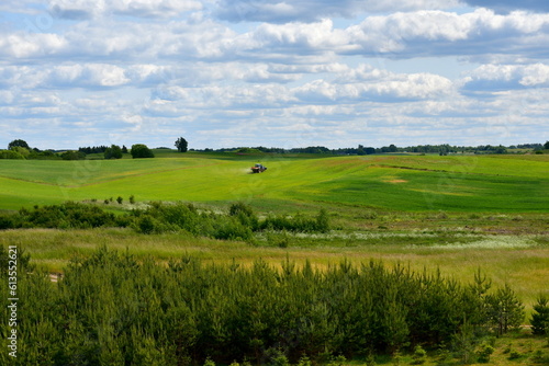 A view from the top of a tall hill covered with grass, herbs, and other flora showing some vast fields, meadows, pasturelands, forest,moors, and a tall hill with some flags on top of it seen in summer