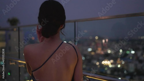 Elegant Asian woman drinking red wine at luxury rooftop bar of city hotel. City view on night.