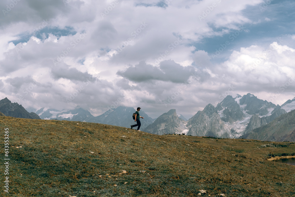 Male hiker walk far in the long distance, on a summer sunny day, against the background of snow-capped peaks of the Caucasus Mountains, Georgia