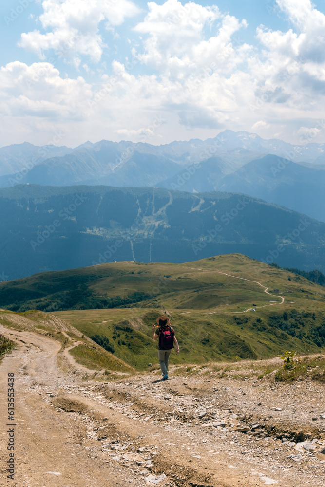 Woman in wide sun hat and backpack, tourist on hiking route to Koruldi Lakes, Svaneti region, Mestia Georgia. The concept of travel and active recreation. Summer day.Vertical photo