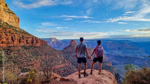 Young couple standing on edge of rock with panoramic aerial view from Bright Angel hiking trail at South Rim of Grand Canyon National Park, Arizona, USA, America. Amazing vista after sunrise in summer
