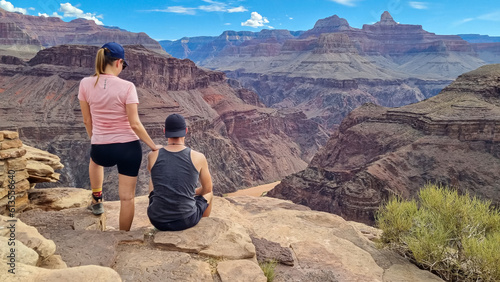 Couple standing at cliff edge with scenic aerial view of Colorado River weaving through rugged terrain seen from Plateau Point, Bright Angel Trail, South Rim, Grand Canyon National Park, Arizona, USA