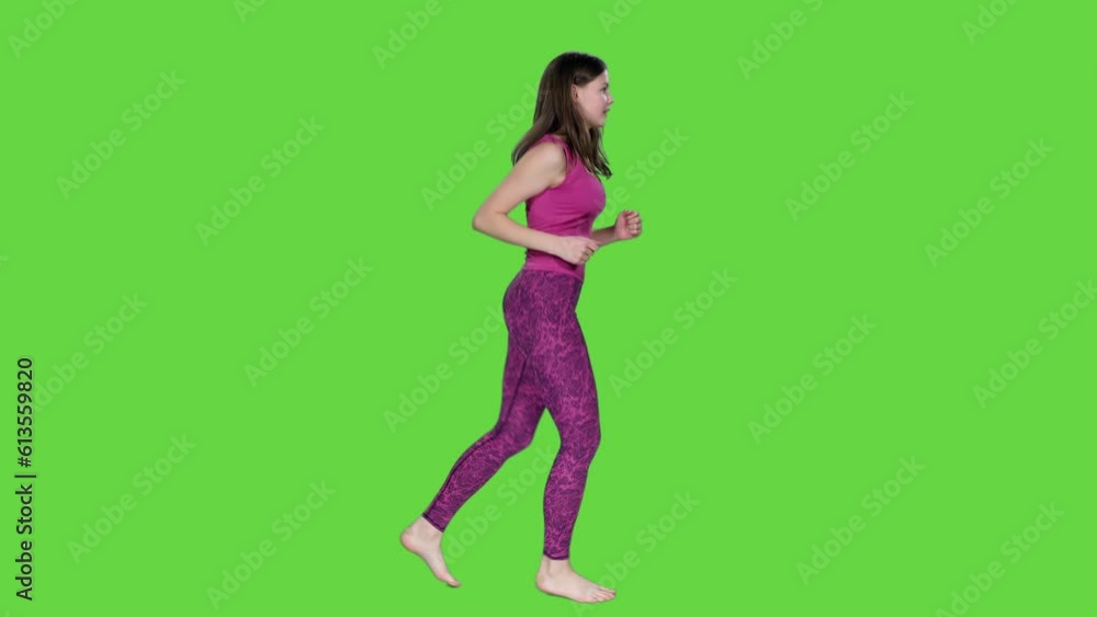 Side view young active woman in pink tank top and leggings jogging barefoot on green background, Chroma key Side view young active woman in pink tank top and leggings jogging barefoot on green background, Chroma key