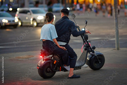 Man and woman riding electric bike in the city. Couple enjoy an evening ride on an electric scooter through the city streets. Couple on electric motor bike riding together