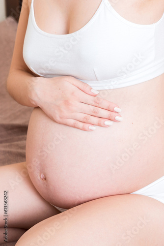 beautiful pregnant woman touching her tummy and keeping one hand on her back at home on bed