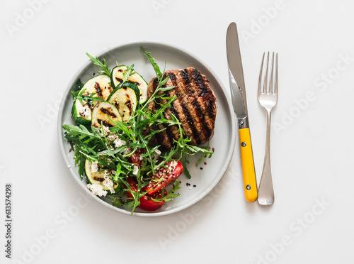 Steak and summer vegetable salad with grilled zucchini, tomatoes and arugula on a light background, top view