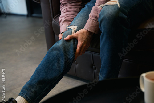 Adult person seated in room suffering from knee pain