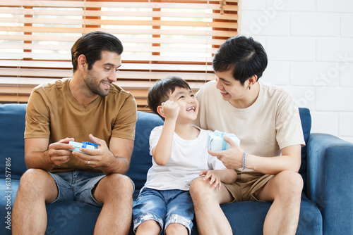 Lovely little boy gives fathers a present in the father's day festival, happy Asian and Caucasian gay couple with foster son. A diversity in gender - LGBTQ and ethnicity concept. photo