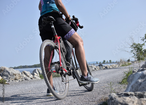 woman riding bike on gravel detail of leg and torso (young south asian, indian rider on bicycle trail) colchester causeway in burlington vermont (brown skin, athletic clothes, cycling jersey, helmet)