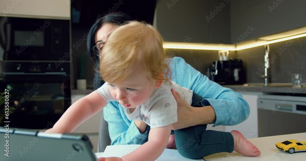 Business woman working online, useing digital tablet and having video call with partners, her little son is sitting next to her, who interferes with her mother's work. Business woman working online, useing digital tablet and having video call with partners, her little son is sitting next to her, who interferes with her mother's work.