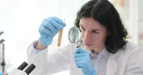 The lab assistant guy looks through the magnifier on the seeds in the flask. Comus suitability for sowing photo