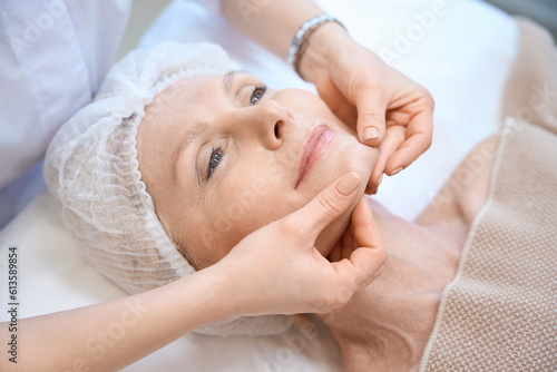 Top view of mature woman in cosmetic cap getting face massage