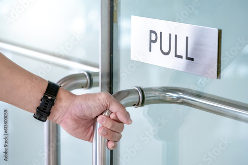 Foto Close up male hand holding stainless steel handle opening glass door in office building
