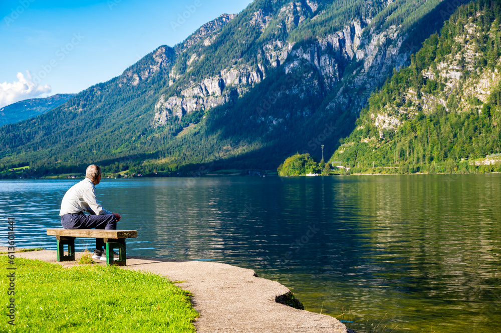 Unidentifiable old men is sitting on bench near the lake in Austrian alps. Concept of relaxation and meditation near nature. Hallstatt city, Austria.