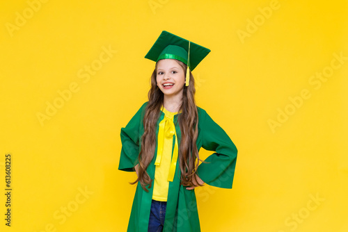 The child is a graduate. A little girl in a graduate hat on a yellow isolated background. Happy graduation to a little girl. Graduation from elementary school.