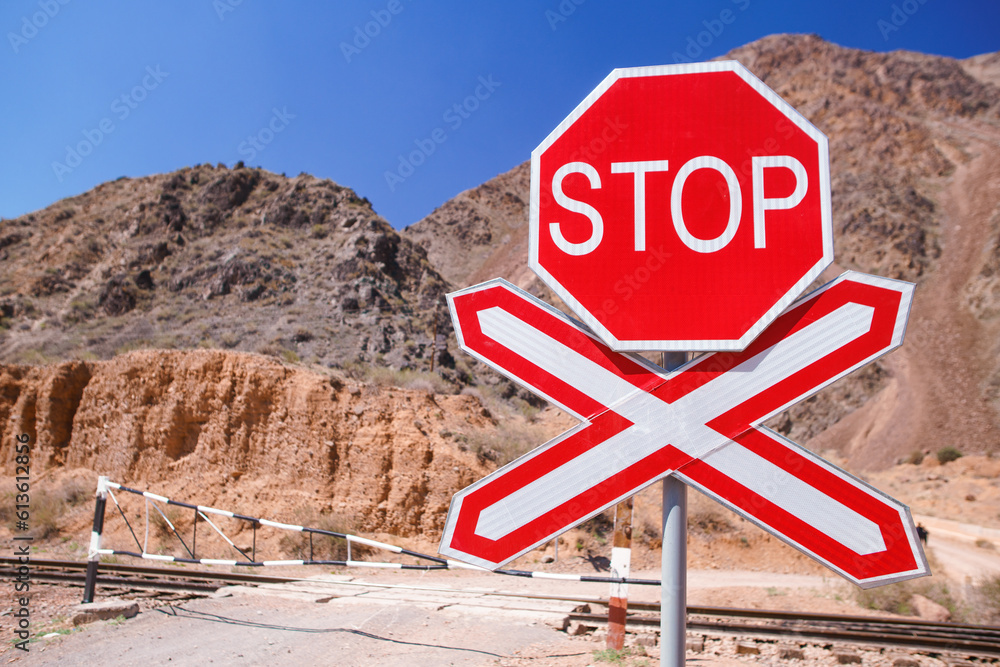 Red Stop sign at a deserted railroad crossing nestled amidst barren, empty terrain against blurred red mountains