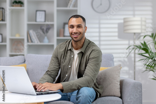 Portrait of a young Latin American freelancer working from home on a laptop. Sitting on the couch and smiling at the camera