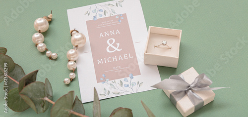Box with engagement ring, earrings and wedding invitation on green background