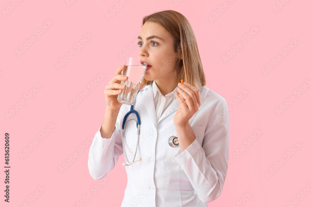 Beautiful doctor with vitamin supplement and glass of water on pink background Beautiful doctor with vitamin supplement and glass of water on pink background