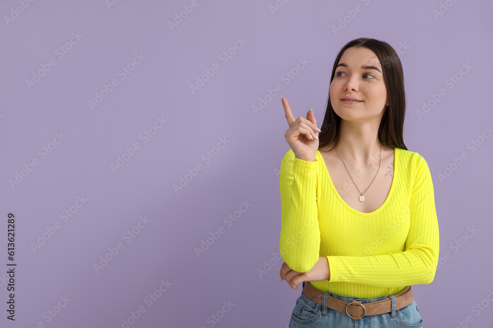 Young woman in bright shirt pointing at something on lilac background Young woman in bright shirt pointing at something on lilac background