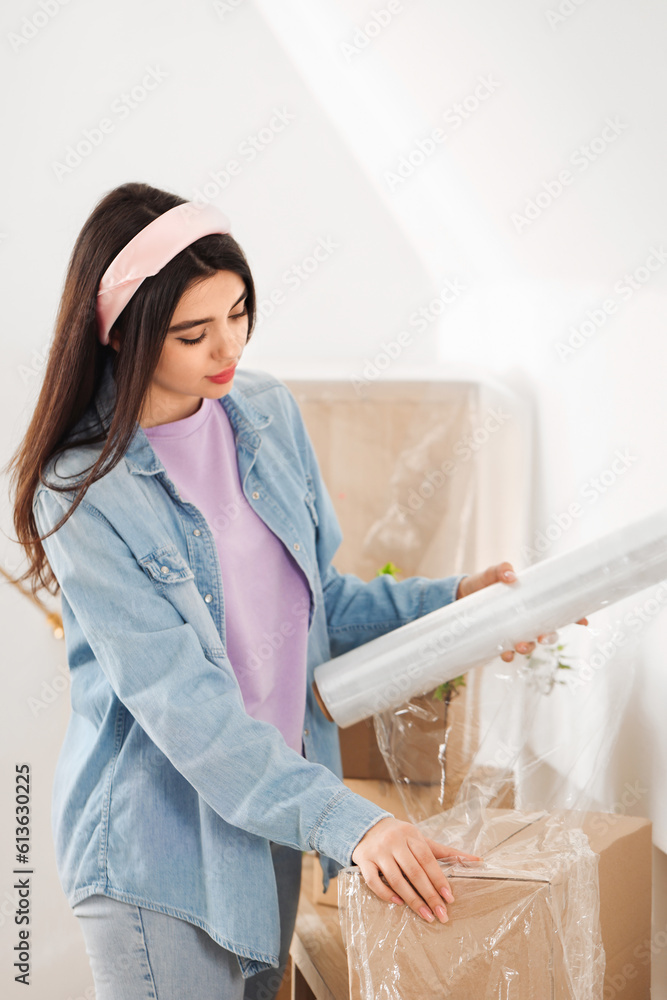 Young woman wrapping cardboard box with stretch film at home on moving day Young woman wrapping cardboard box with stretch film at home on moving day