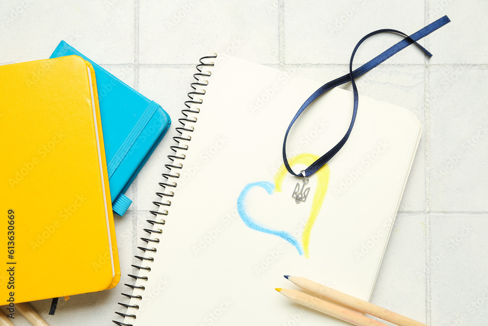 Ribbon with Ukrainian coat of arms, notebooks, drawn heart and pencils on white tile background Ribbon with Ukrainian coat of arms, notebooks, drawn heart and pencils on white tile background