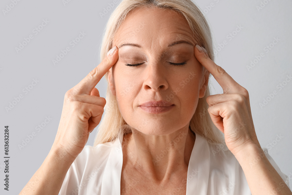 Mature woman doing face building exercise on light background, closeup Mature woman doing face building exercise on light background, closeup