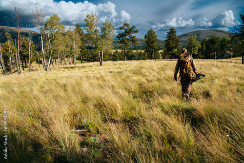 A hunter in camouflage and wearing a backpack walks through a field while bowhunting in the Valles Caldera National Preserve, New Mexico photo