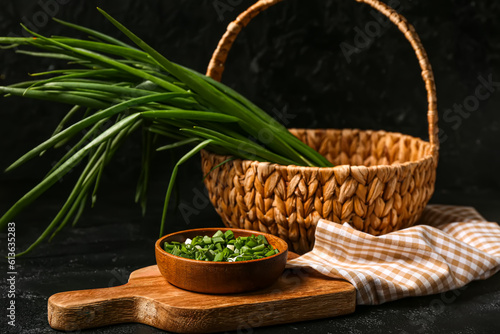 Wicker basket and bowl with fresh green onion on dark background