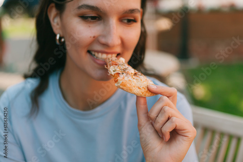 Happy young woman eating pizza in street cafe. Closeup. Street food concept