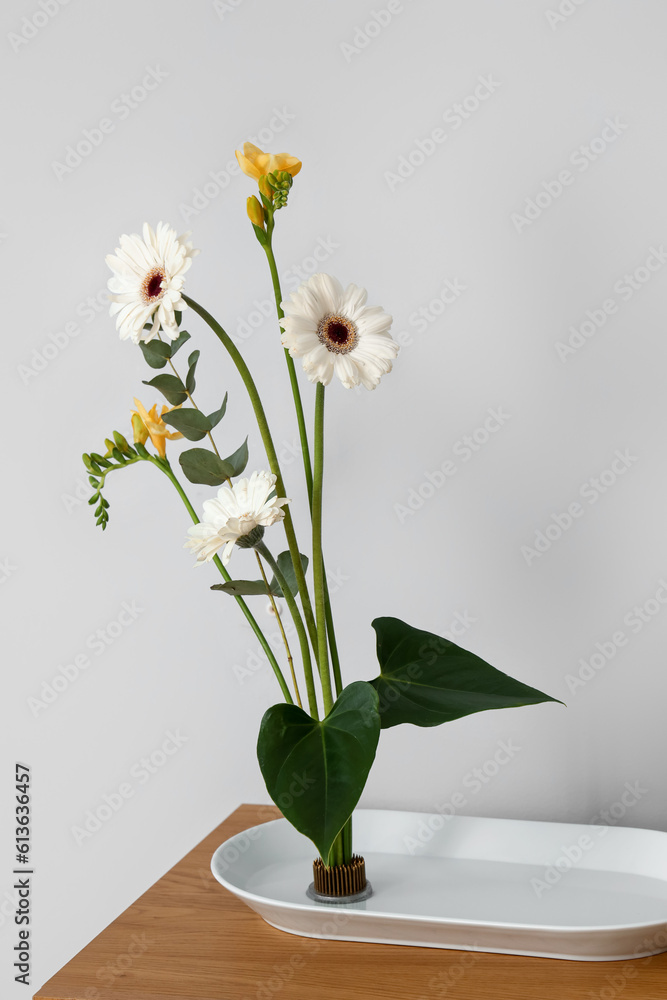 Beautiful ikebana on table near light wall Beautiful ikebana on table near light wall