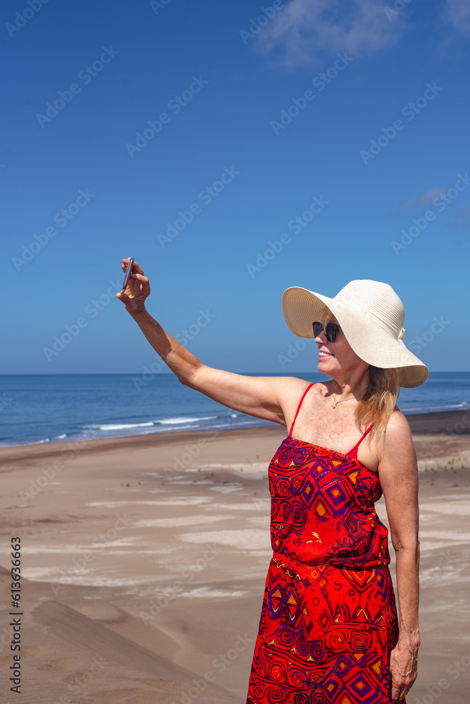 Portrait of cheerful mature woman smiling while taking selfies with mobile phone at the beach. Summer and technology concept. Portrait of cheerful mature woman smiling while taking selfies with mobile phone at the beach. Summer and technology concept.