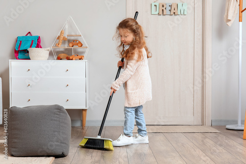 Foto Cute little girl sweeping floor with broom at home